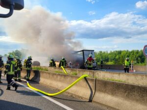 Feuerwehr bekämpft mit Wasserschläuchen Brand eines Lkw-Aufliegers auf der Autobahn