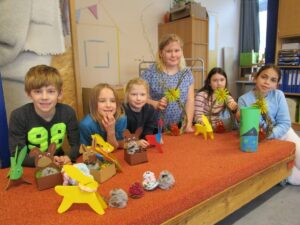 Sechs Kinder in der Kita Unterwallweg präsentieren gebastelte Osterdekorationen aus Papier, Wolle, Zweigen und Pappe auf einem Tisch.