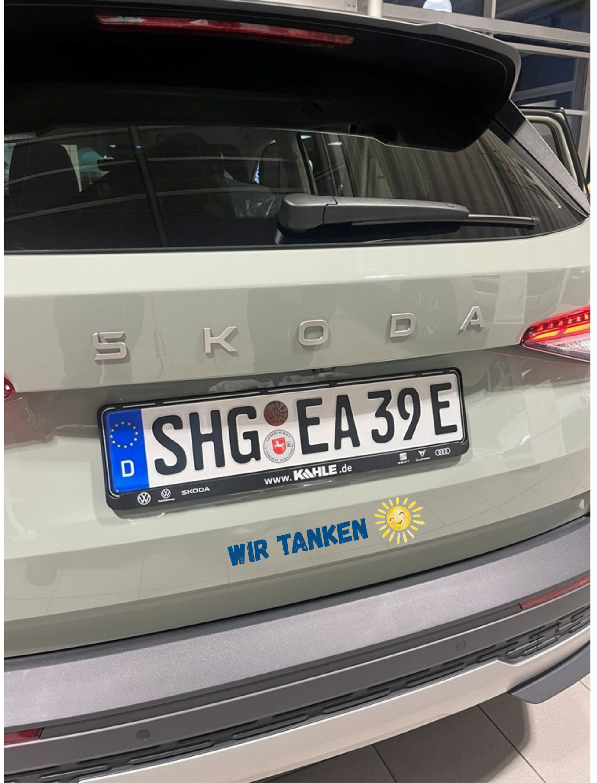Heckansicht eines grauen Skoda mit Aufkleber 'WIR TANKEN' und Sonnensymbol.
