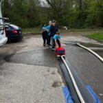 Ein kleines Auto wird auf einem Feuerwehrschlauch über den Asphalt geschoben.