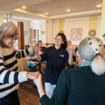 Eine Frau tanzt gemeinsam mit Seniorinnen in einer Gruppe.