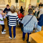 Personen, teilweise in Rollstühlen, befinden sich in einem Gemeinschaftsraum.