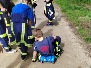 Kinder in Feuerwehrkleidung fahren mit einem blauen Bobbycar durch einen Parcours.