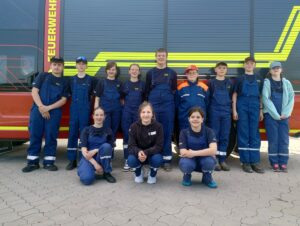 Eine große Gruppe von Kindern in blauen Feuerwehruniformen posiert vor einem roten Feuerwehrfahrzeug.