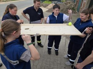 Kinder halten ein Holzbrett mit Seilen, um einen Tennisball zu balancieren.