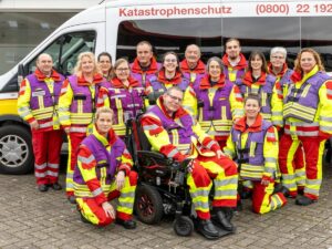 Gruppe von ASB-Einsatzkräften in rot-gelber Warnkleidung vor einem weißen Katastrophenschutz-Fahrzeug.