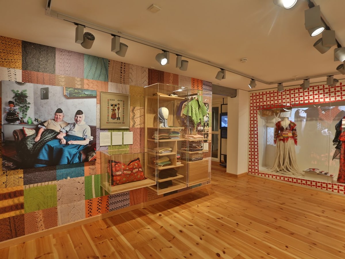 Museumsausstellung mit historischen Trachten und Stoffmustern an der Wand.