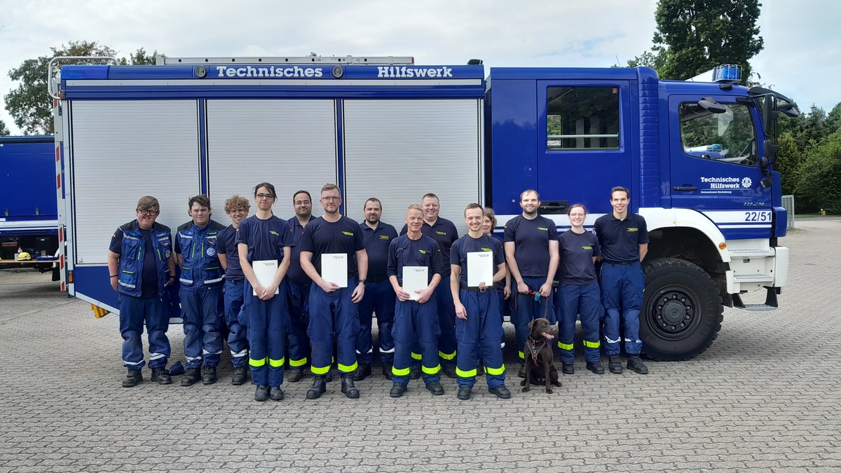 Eine größere Gruppe von THW-Helfern posiert vor einem blauen Einsatzfahrzeug.