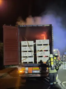 Feuerwehrkräfte unter Atemschutz am geöffneten Lkw-Container mit brennender Lithium-Ionen-Batterieladung auf dem Rastplatz Auetal Süd