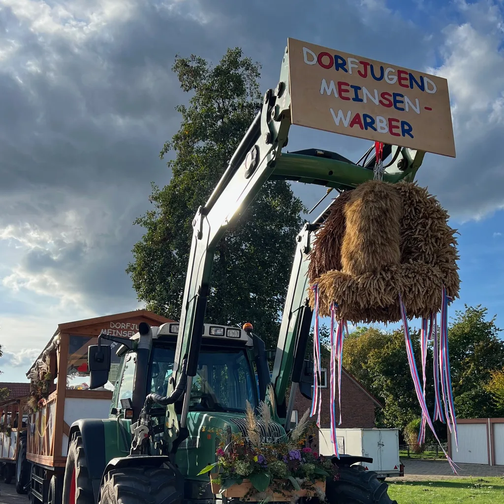 Grüner Traktor mit Erntekrone und Schild der Dorfjugend Meinsen-Warber vor einem geschmückten Erntewagen
